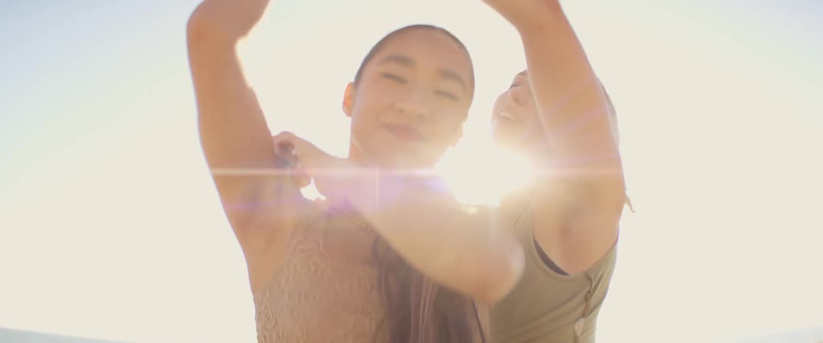 Portrait of two women dancing with their hands and the sunlight in the background