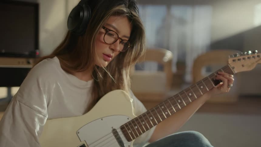 Young woman with headphones playing the guitar