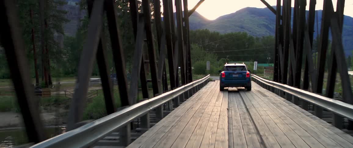 Blue car crosses a wooden bridge at sunset