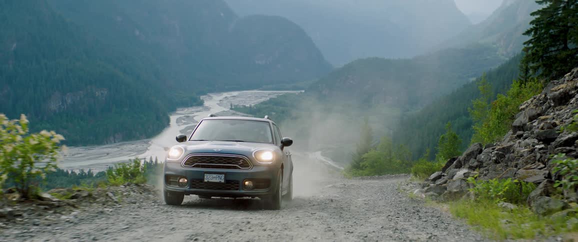 Car drives along sloping mountain road overlooking river on a foggy day