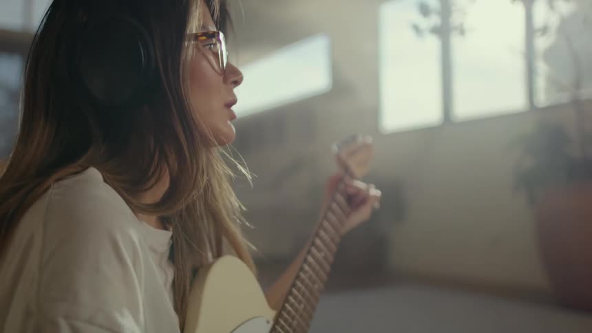 A young woman playing the guitar with headphones in her ears
