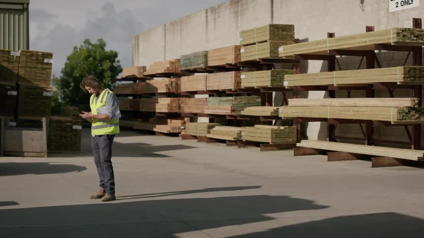 A man is using his cell phone in the lumber yard