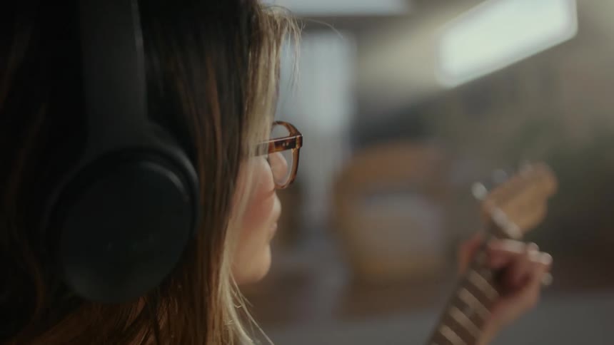 A woman wearing glasses playing guitar while wearing headphones
