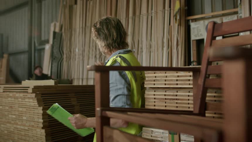 Man wearing safety vest stands in warehouse near lumber and motions with his hand