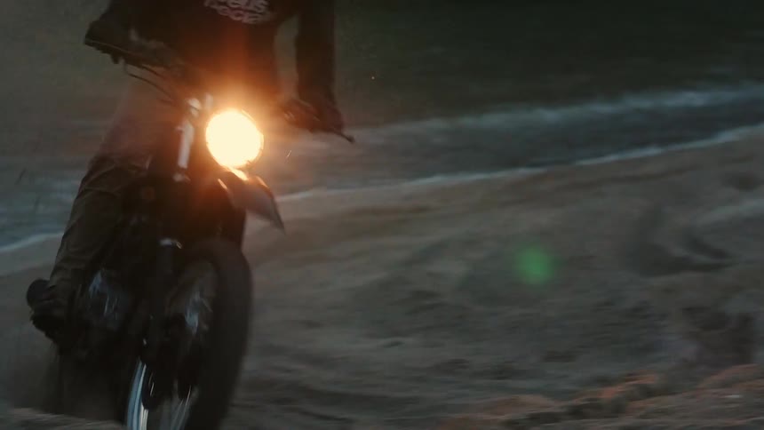 A man races his dirt bike on a beach