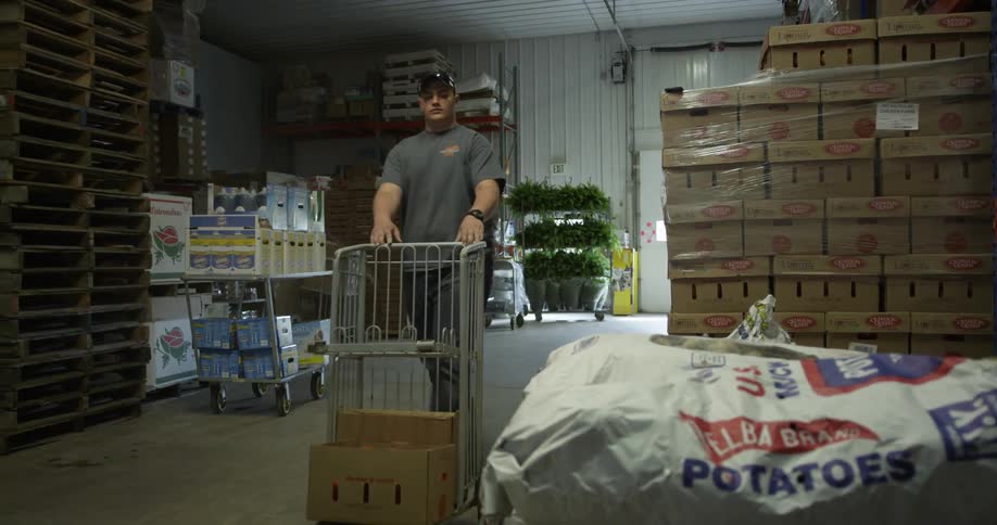 Man pushes a cart then lifts large sack of potatoes