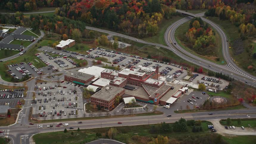 A big building along the freeway with many parked cars in its premises