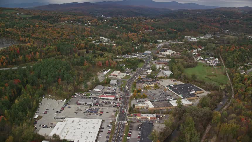 Highway passes through town bordered by deciduous forest in the fall