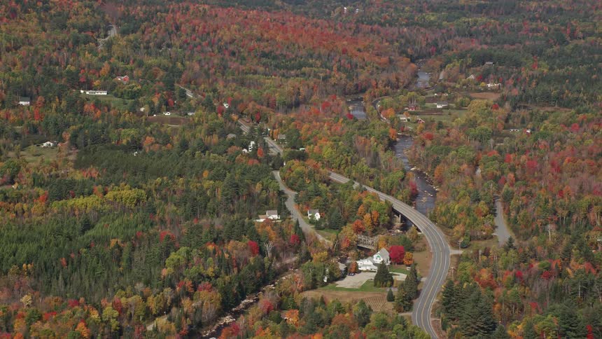 Aerial view of a car crossing a bridge over a river in a forested area during the fall