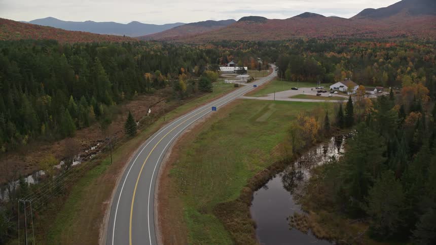 Aerial of a tarred road and isolated buildings on both sides at midday