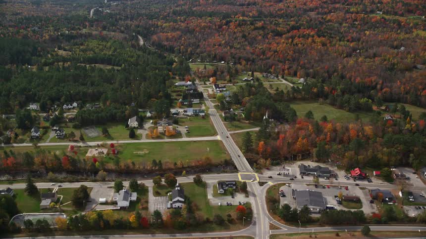 An aerial view of a rural region with some houses and several forests around