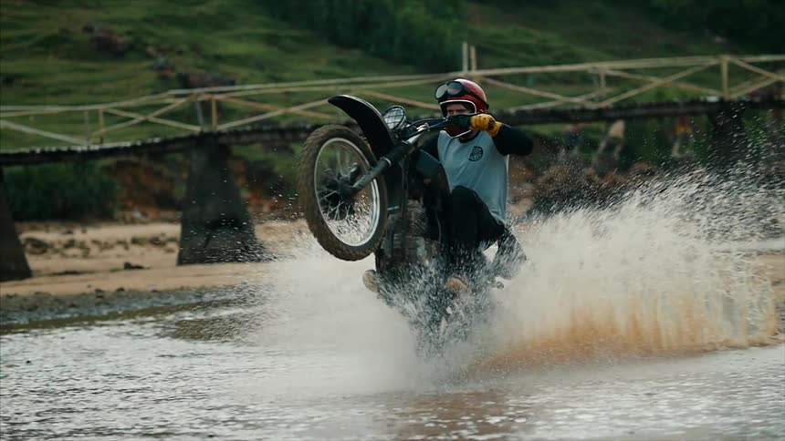 A man riding a dirt bike through water and popping a wheelie