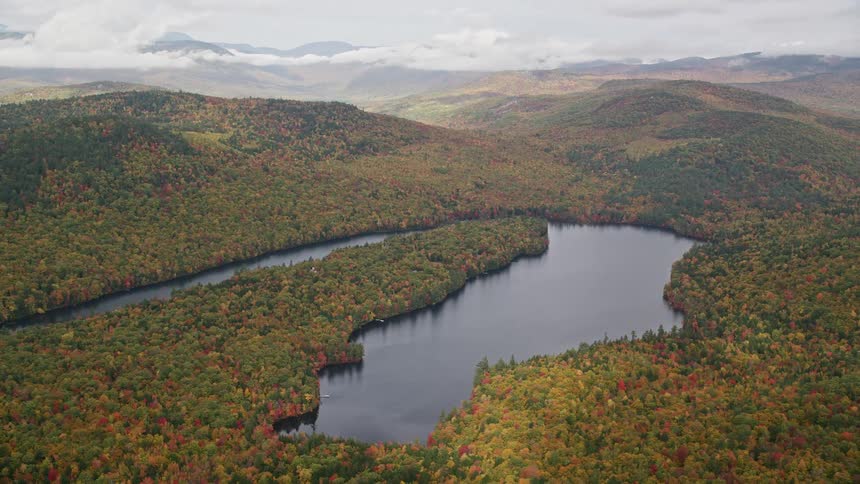 A horseshoe lake is surrounded by hills and an autumn forest on a cloudy day