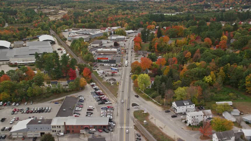 Aerial of moving cars parked cars and road side buildings at midday
