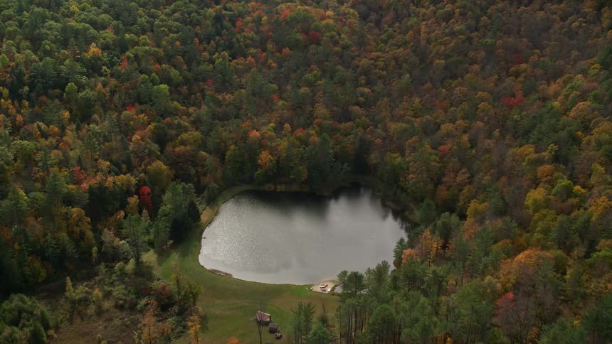 An aerial panorama of mountains with forests and a small lake at the base