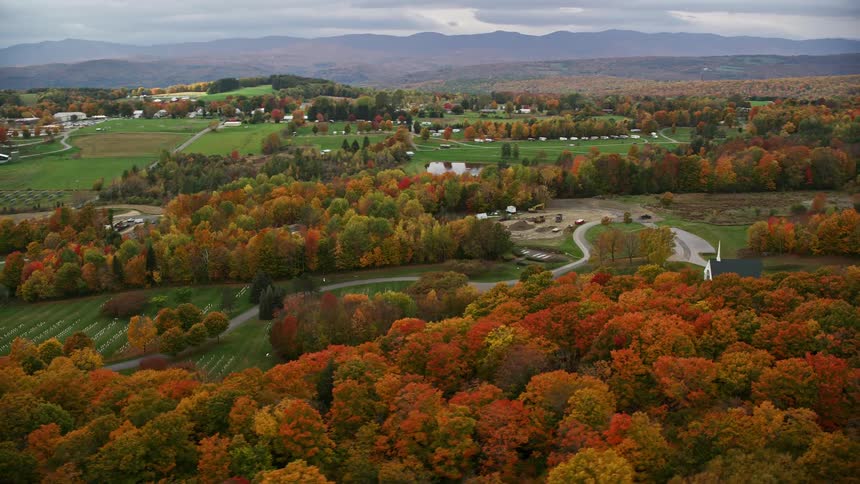 A rural area with some houses and forests around with trees changing the color of their leaves to orange