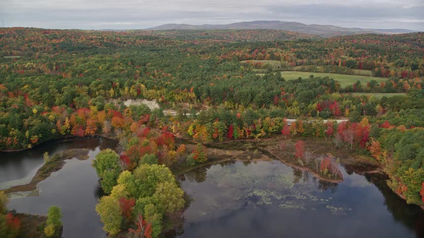 Aerial of a shallow lake and a golf course surrounded by an autumn forest