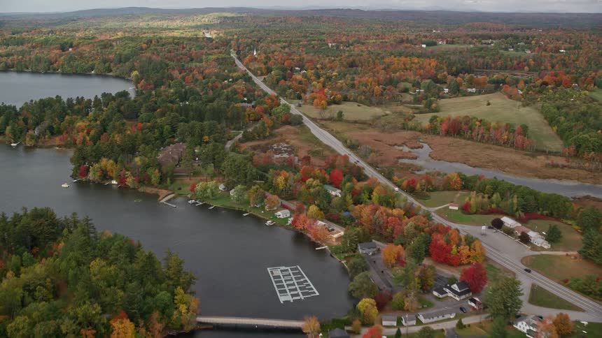 A large road that passes through a rural area with a lake on the left and many trees around