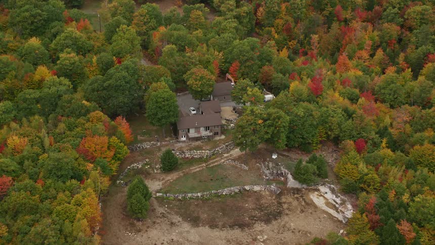 House surrounded by forest in fall foliage sits near road leading toward lake