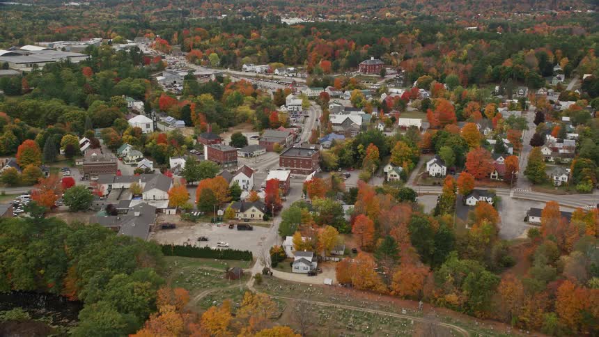 A sub urban town with lots of building surrounded by trees as cars go b the road