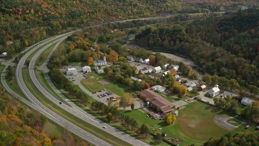 Aerial view of cars driving on highways near a town in the forested area during autumn