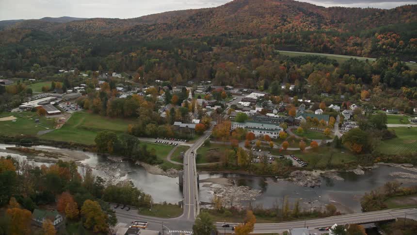 A modest bridge crosses the white river close to a rural town on a cloudy autumn day