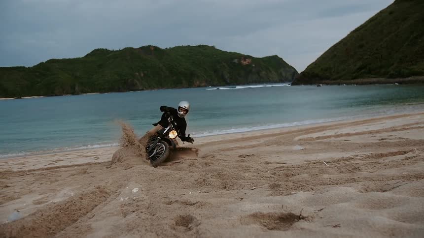 Person rides dirt bike through the beach sand