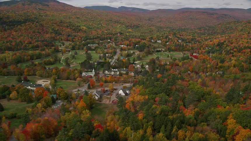 A small village with small houses in the middle of a large forest with trees changing the color of their leaves to orange