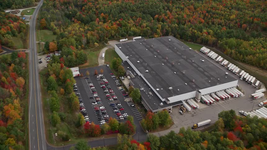 A large building with a parking lot full of cars and around it there are just forests