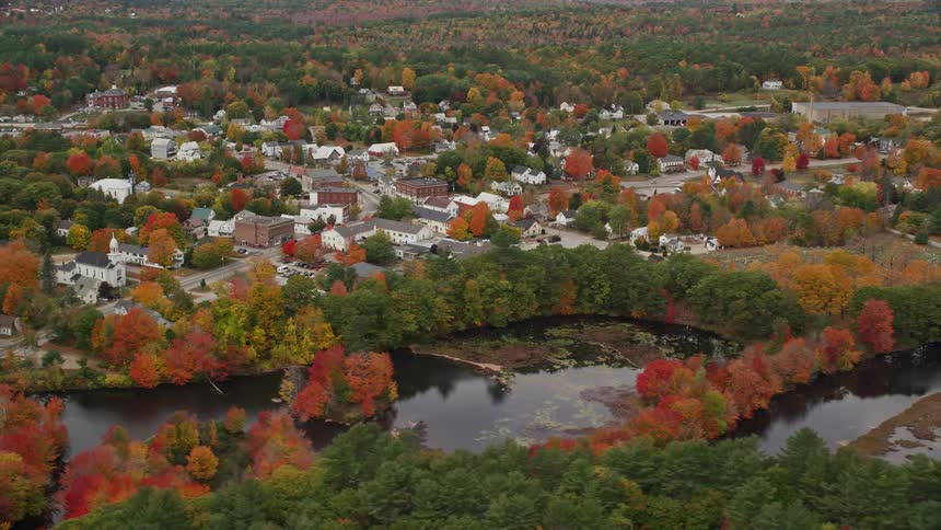 A panorama of a rural town with a river and several trees that are changing the colors of their leaves