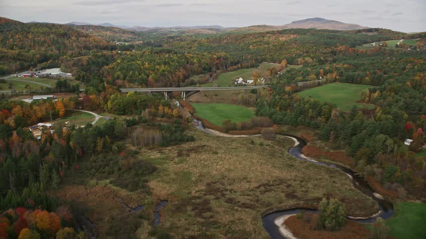 Aerial view of a car crossing a bridge over a river in a forested area during the fall