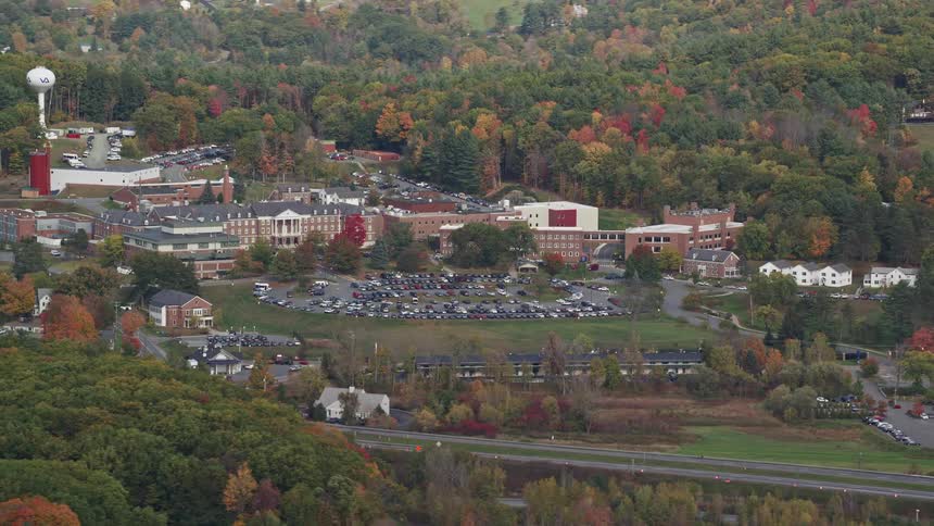 A suburban region with a few buildings with parking in front and several trees around