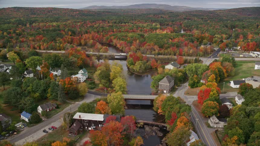Bridges cross river running through town and encompassing deciduous forest during the fall