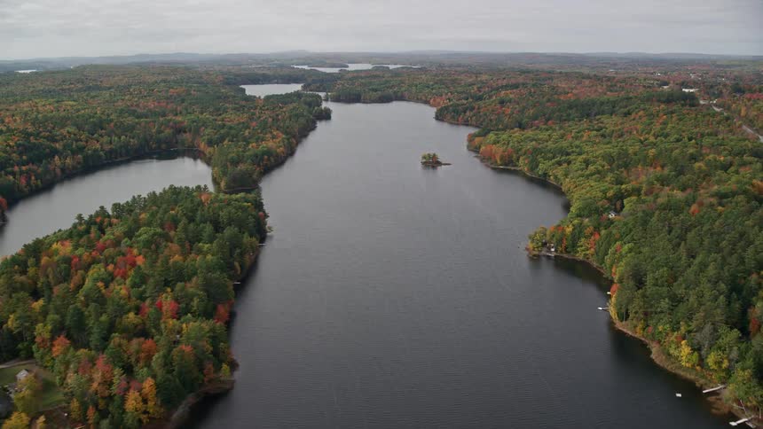 Aerial of a lake surrounded by an autumn forest on a cloudy day