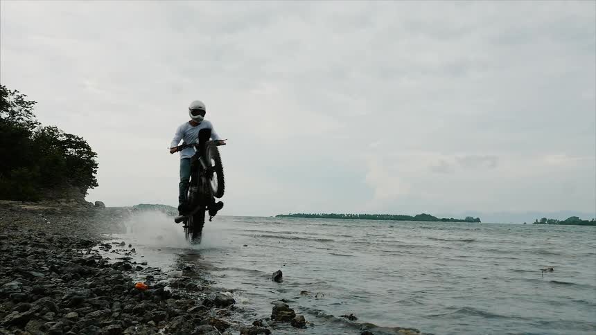 Rider on motorcycle does a wheelie through the water