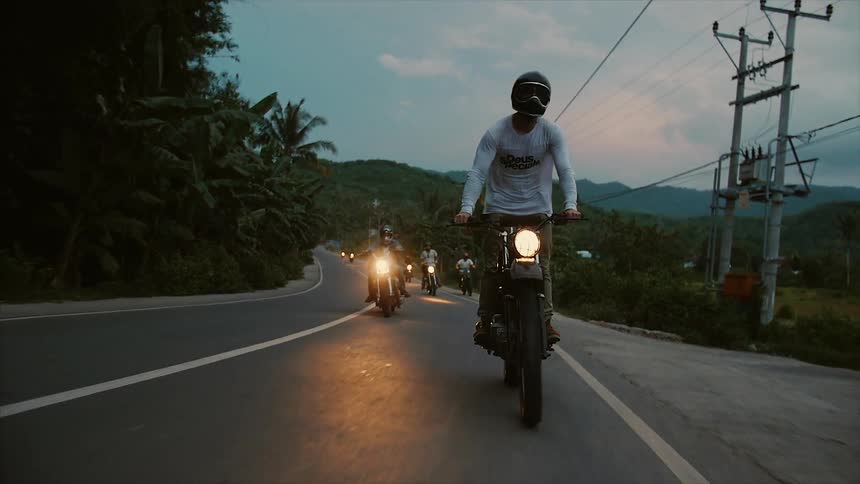 People are lined up riding motorcycles on a small road