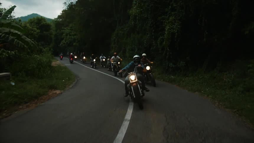 A long line of people riding motor bikes down a mountain road at sunset