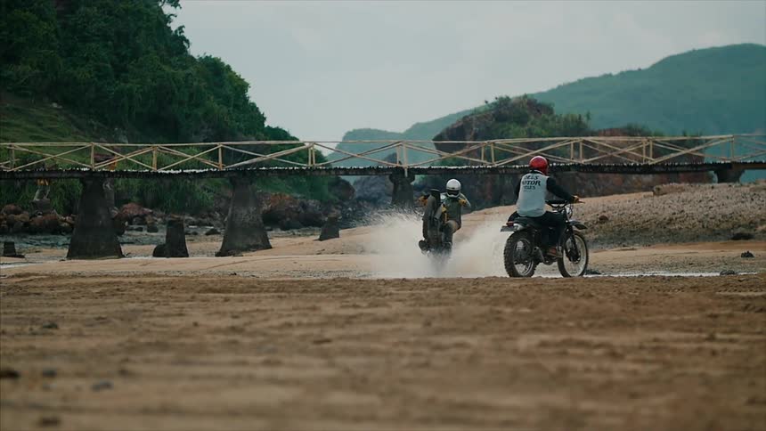 Two people ride dirt bikes through water doing wheelies
