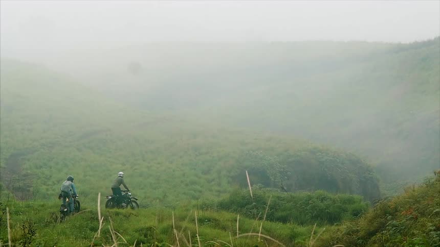Motorcyclists riding a trail through some green hills on a foggy day