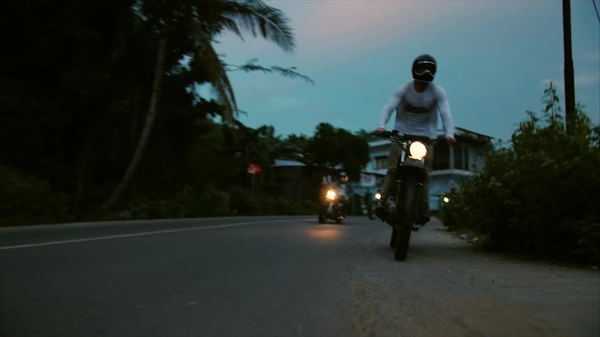 A group of people ride motorcycles on the road at sunset