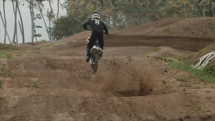 Dirt flies in the air as a person does jumps over hills on a dirt bike