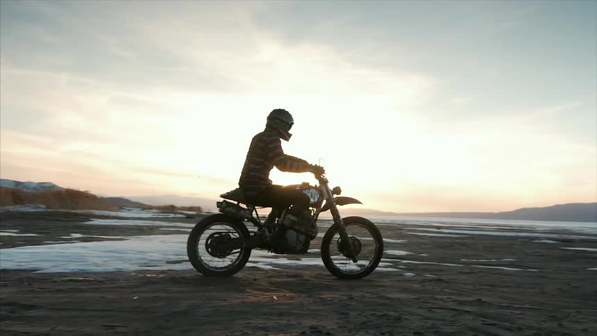 A man riding over dirt and snow on a dirt bike at sunset