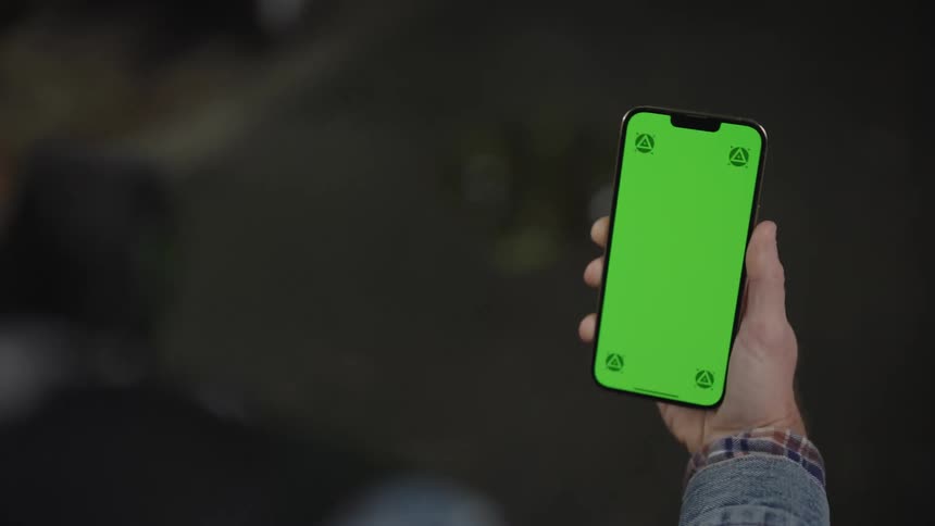 A man holding a mobile device with a green screen on while walking