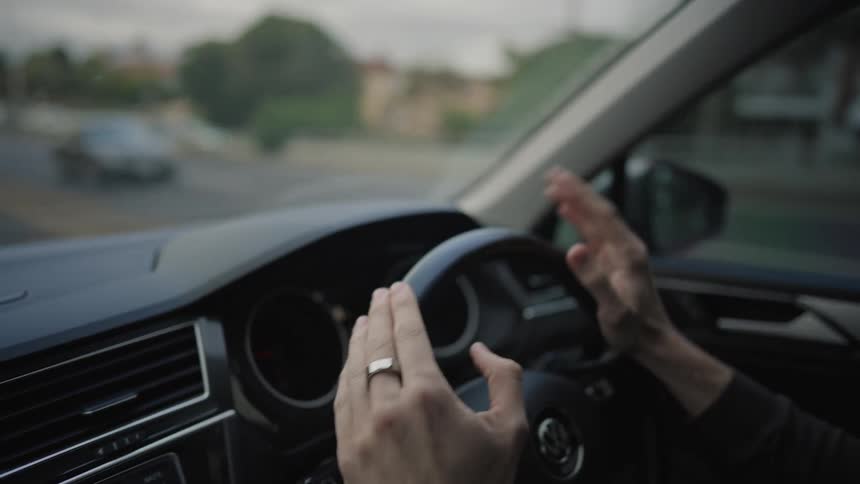 Internal view of a persons vehicle with hands tapping to the rhythm of music on the steering wheel while driving