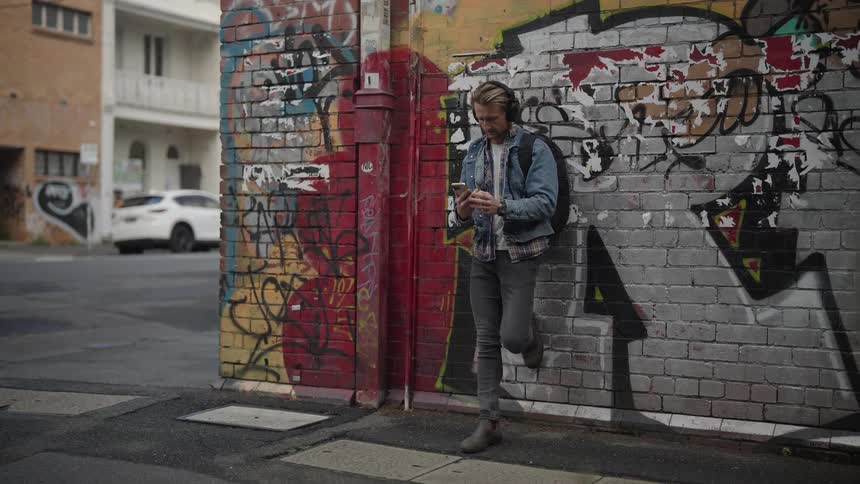 Man listens to music reclined on a wall in the city streets