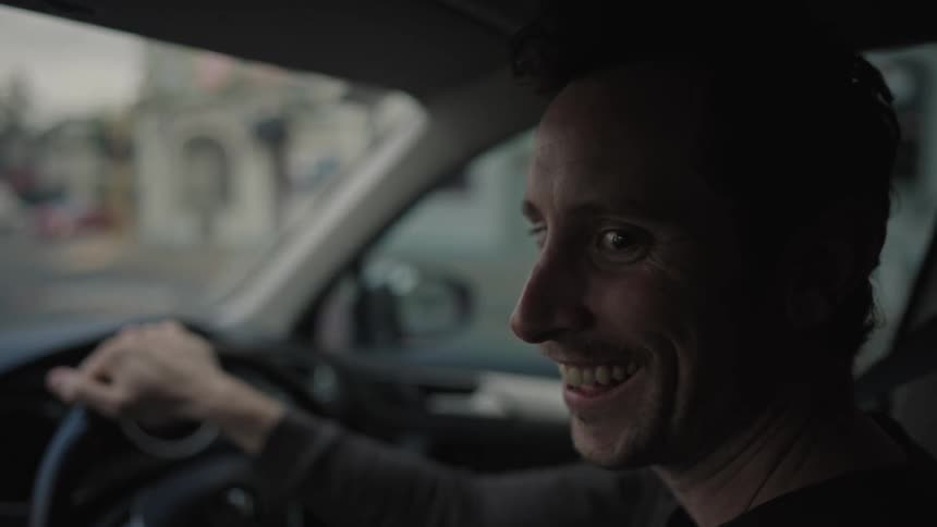 Man sits in a car talking and laughing