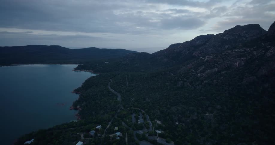 A huge mountain faces a lake with still water and there is a road nearby