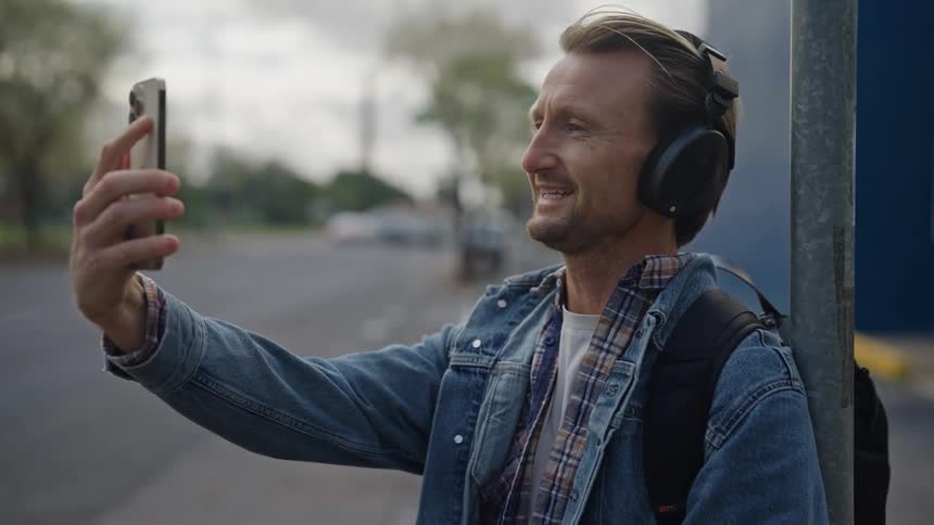 Portrait of a man with headphones answering a video call and smiling while talking in an outdoor setting