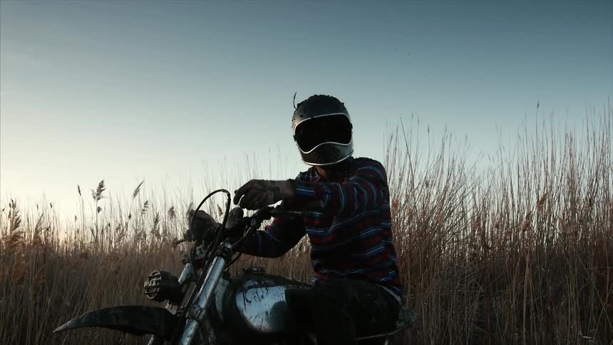 A man is sitting on a motorcycle in front of a field of tall grass