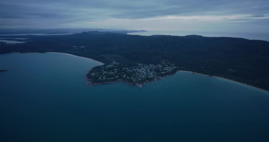 Aerial of a small island in the ocean with mountains at dusk
